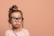 Curious Little Girl with Glasses Pouting on Peach Background