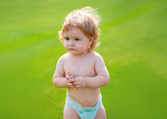 Sticker - Happy baby in diaper having fun at the park. Funny baby child. Funny little child closeup portrait on green grass background.