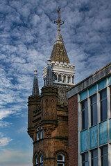 Wall Mural - Historic tower with spire against a dramatic cloudy sky, juxtaposed with modern building facade in Leeds, UK.