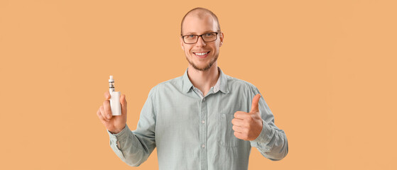 Wall Mural - Young man in eyeglasses with disposable electronic cigarette showing thumb-up on beige background