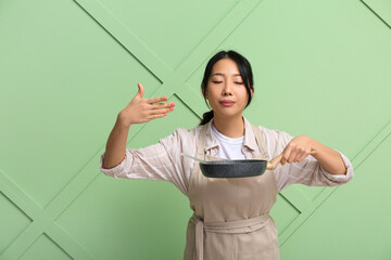 Wall Mural - Portrait of young Asian woman with frying pan on green background