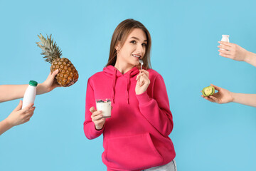 Wall Mural - Thoughtful young woman and hands holding yoghurt with fruits on blue background