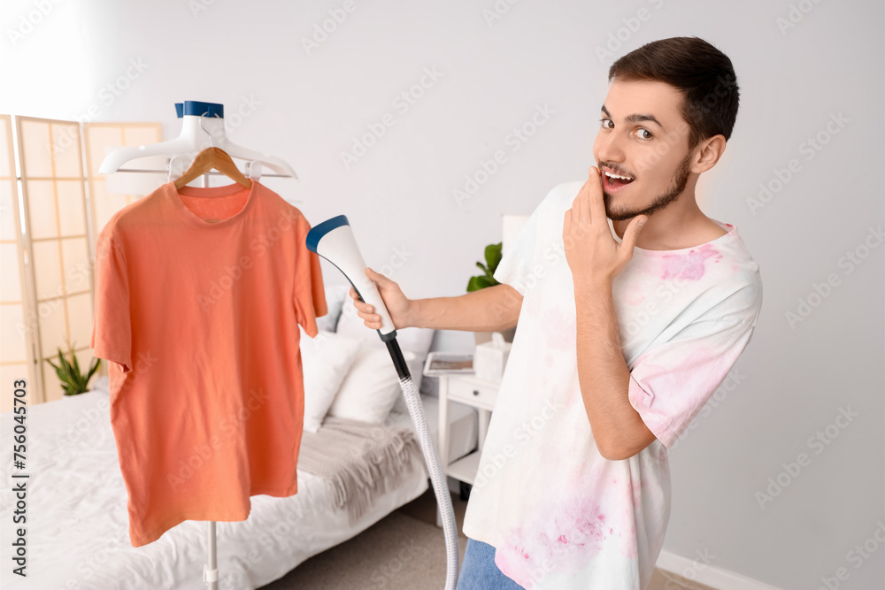 Shocked young man steaming orange t-shirt at home