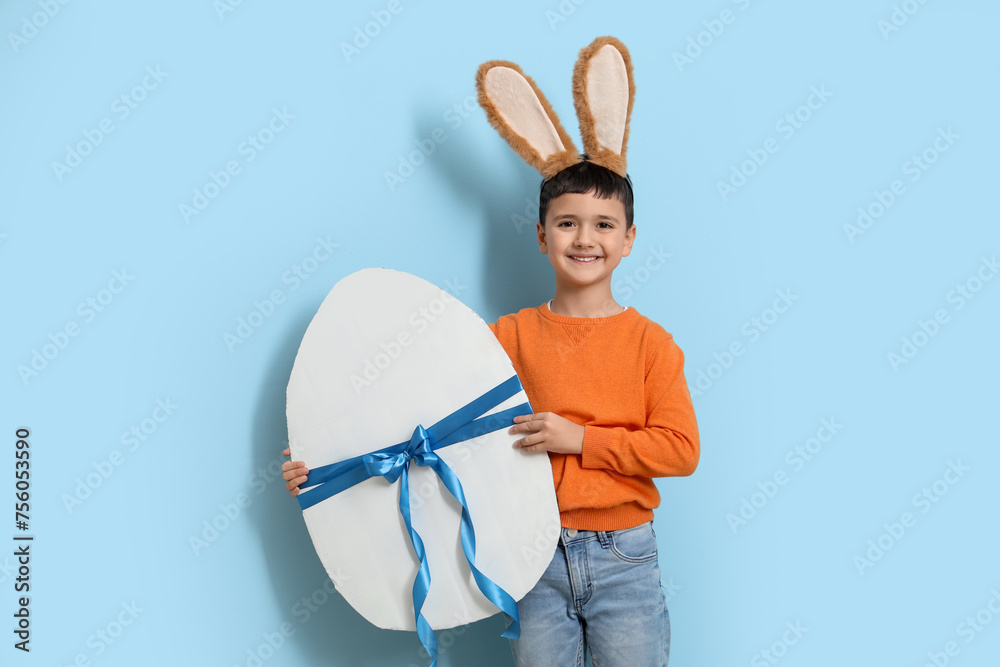 Cute little boy with bunny ears and big Easter egg on blue background