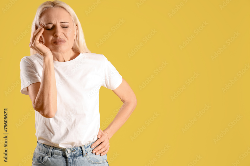 Mature woman suffering from headache on yellow background