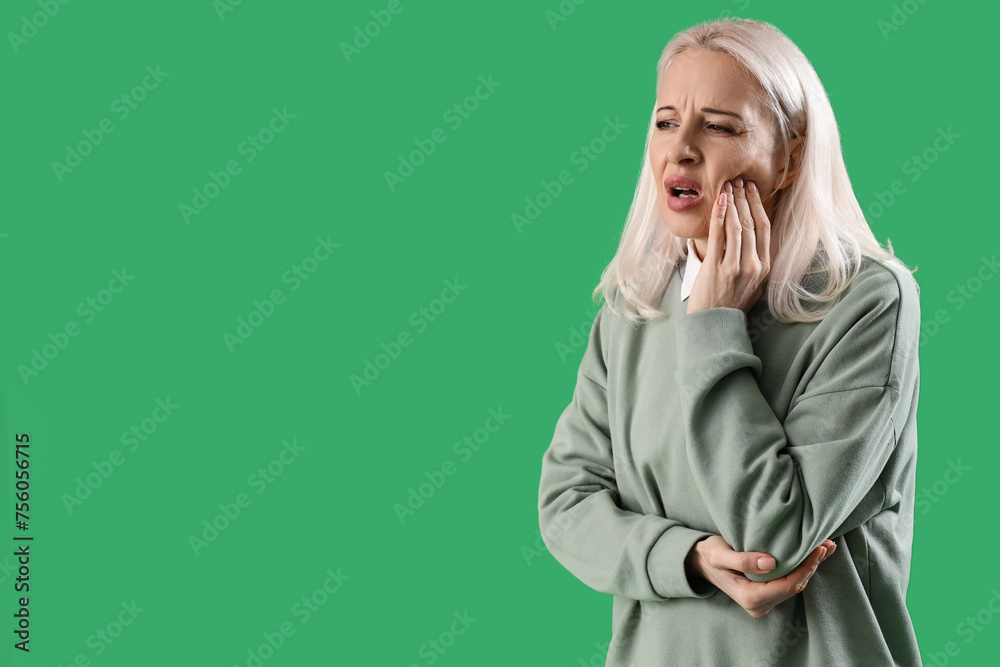 Mature woman suffering from toothache on green background