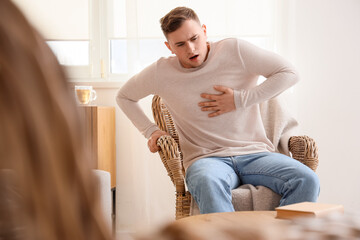 Wall Mural - Young man suffering from chest pain in armchair at home