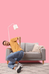 Canvas Print - Young man suffering from back pain near sofa on pink background