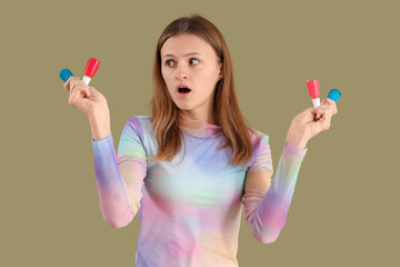 Wall Mural - Young woman with bottles of nail polishes showing surprise on green background