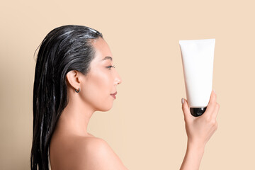 Poster - Young Asian woman with tube of hair mask on beige background, closeup