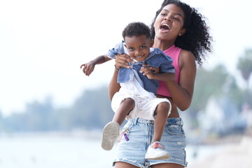 Wall Mural - Mixed race African and Asian mother and boy is playing at the outdoor area. smiling happy family have fun running on the beach. portrait of mom and kid lifestyle with a unique hairstyle.