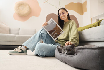 Sticker - Young woman reading magazine and cute British Shorthair cat in pet bed at home