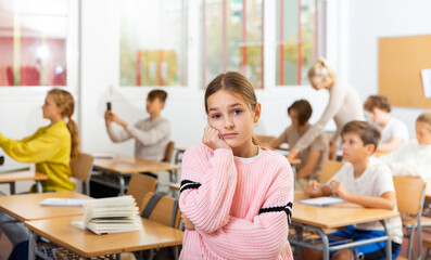 Wall Mural - Portrait of unhappy kid girl studying in classroom at secondary school, learning lessons