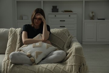 Wall Mural - Sad young woman sitting on sofa at home, space for text