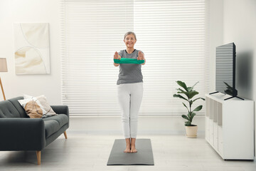 Sticker - Senior woman doing exercise with fitness elastic band on mat at home