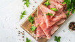 A wooden board with slices of tasty ham, peppercorns, and greens on a light background.