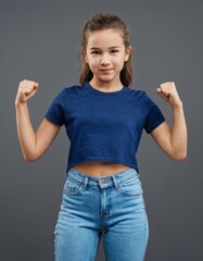 Wall Mural - A young preteen or teen girl is standing with her arms raised in the air, wearing a blue shirt and blue jeans. She has a smile on her face and she is happy or excited