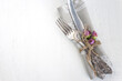 Festive place setting for Easter dinner; Vintage fork and knife, dry pink roses flowers on arustic wooden background
