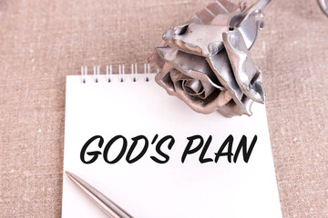 God's Plan, the text is written in a notebook lying on a linen linen and an iron rose flower.