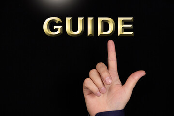 Wall Mural - GUIDE text, a word written on a black background pointed to by a hand with the index finger of a person.