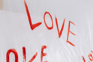 Multiple drawings of the word LOVE hand-painted in bright red forming a pattern on a plain white surface oilcloth, Valentine`s day concept celebration decoration in photo studio. Love, holiday, party
