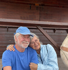 Wall Mural - Portrait of senior caucasian couple exchange cuddles sitting together in outdoors enjoying vacation and retirement