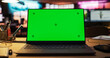 © Gorodenkoff - Laptop Computer with Green Screen Standing on a Wooden Desk with Height Adjustable Function. Chroma Key Display in Empty Decorated Creative Office for Game Development Startup