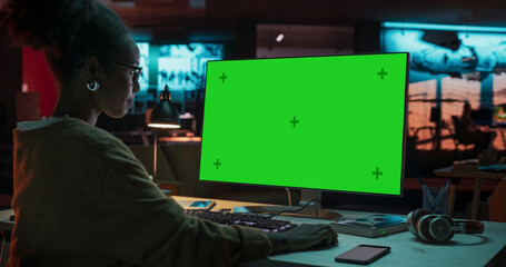 Fototapete - Portrait of Creative Black Woman Sitting at Her Desk Using Desktop Computer with Mock-up Green Screen. Female Specialist Working at Night in Game Development Startup, Finishing Details on a Project