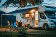 A family spends quality time together outside their RV at a campsite during a calm evening under the twilight sky