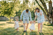 © Serhii - Mother, father hold hands happy children daughter. Running in green grass in nature on summer day. Concept of family spending time together on a picnic. Mom, dad, and kids walking in park at sunset.
