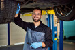 © bnenin - Portrait of a mechanic standing under the car and smiling for the camera, holding a lamp, and checking a tire.