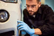 © bnenin - A mechanic checking a scratch on the car, wearing gloves.