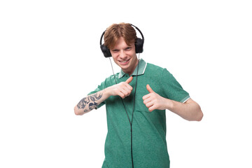 young positive red-haired caucasian guy in a green t-shirt listens to music with headphones