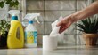 A hand reaching for a roll of paper towels next to a bottle of all-purpose cleaner.