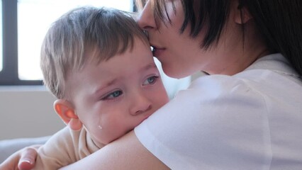 close up portrait of a crying toddler with tears on face, sitting on mother hands. mom strokes, embr