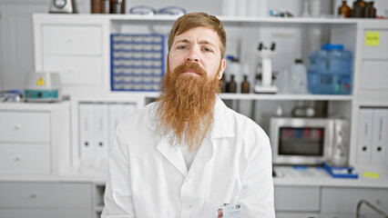 Young redhead man scientist sitting with serious face at laboratory