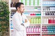Handsome hispanic man working at pharmacy drugstore looking to the side with arms crossed convinced and confident