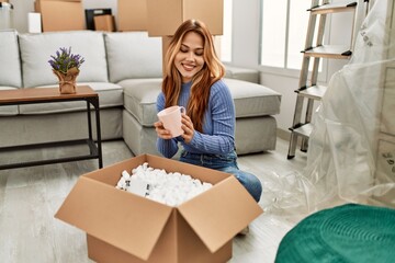 Wall Mural - Young caucasian woman smiling confident unpacking cardboard box at new home