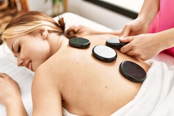 Poster - Young caucasian woman lying on table having back massage using hot stones at beauty salon