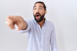 Hispanic man with beard wearing casual shirt pointing with finger surprised ahead, open mouth amazed expression, something on the front