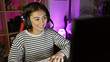 © Krakenimages.com - A smiling young hispanic woman wearing headphones uses a computer in a colorful gaming room at night.