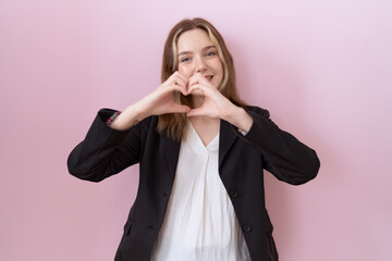 Wall Mural - Young caucasian business woman wearing black jacket smiling in love doing heart symbol shape with hands. romantic concept.