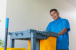 © Mdv Edwards - A dedicated middle-aged male janitor in a blue uniform pushes a cleaning cart along a bright hallway.