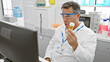 Middle-aged man in lab coat examining a specimen in a medical laboratory setting while wearing safety goggles.