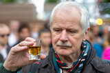 Fototapeta Dmuchawce - Senior man looking skeptical at a glass of alcohol.