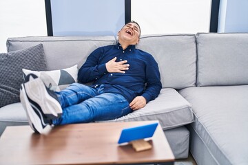 Sticker - Young latin man watching movie on touchpad sitting on sofa at home