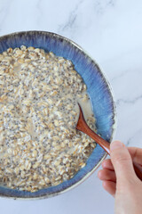 Wall Mural - Female hand holding spoon and eating oatmeal breakfast bowl with chia seeds and plant-based milk. Top view. Close-up. Organic vegan food, healthy dieting concept.