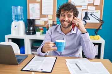 Canvas Print - Young hispanic man business worker relaxed talking on smartphone drinking coffee at office