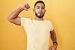 Young hispanic man standing over yellow background stretching back, tired and relaxed, sleepy and yawning for early morning