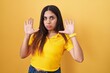 © Krakenimages.com - Young arab woman standing over yellow background moving away hands palms showing refusal and denial with afraid and disgusting expression. stop and forbidden.